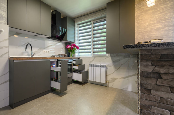 Real showcase interior of small modern trendy gray kitchen, drawrs retracted to show inside - Foto, afbeelding