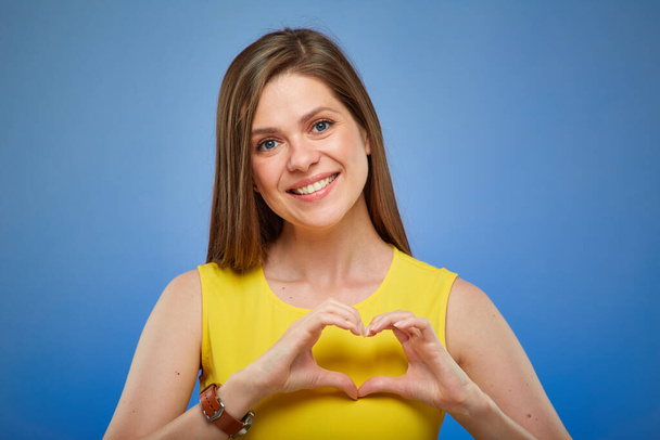 Woman smiling and doing heart gesture with fingers. Isolated female portrait on blue background. - Foto, Imagen