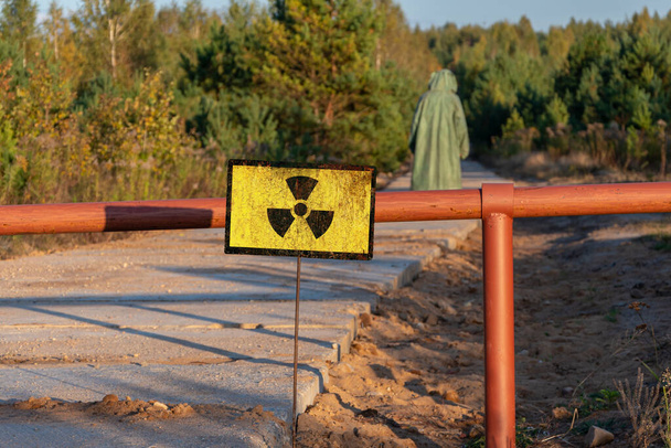 знак радіаційної небезпеки на тлі лісу і дороги, російський військовий під час хімічного захисту входить в зону радіоактивного забруднення., - Фото, зображення
