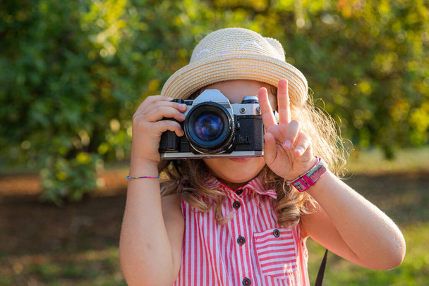 A little girl with a camera takes pictures and makes the V sign with her fingers, photographer concept - Foto, afbeelding