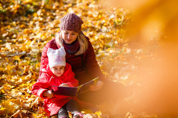 mother teaching daughter in autumn park, Mother teaching daughter to read. - Foto, afbeelding