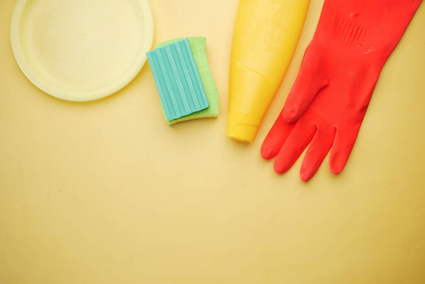 σφουγγάρι, λαστιχένια γάντια και πολύχρωμο πιάτο σε κίτρινο φόντο , - Φωτογραφία, εικόνα