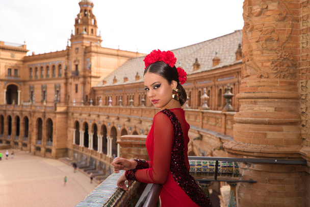 Прекрасна дівчина - підліток танцює фламенко на балконі квадрата в Севільї. Вона носить червону сукню з рофлями з великою кількістю мистецтва. Культурна спадщина фламенко людства. - Фото, зображення