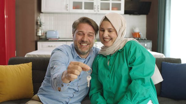 The headscarved woman and her husband happily hold the keys to their new property. Portrait proud happy young adult couple smiling while holding keys in their new flat. Valentine's Day gift concept. - Photo, Image
