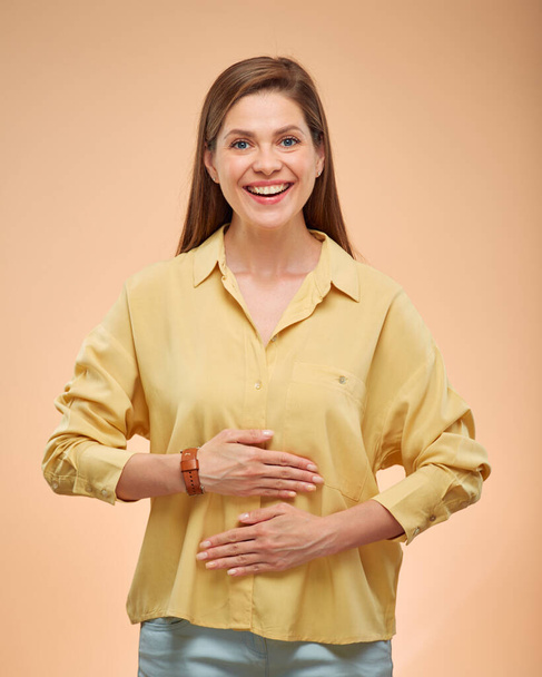 Smiling woman holding hands on stomach, isolated portrat on studio yellow background. - Valokuva, kuva