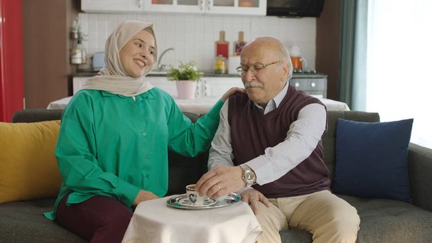 Χαρούμενος στοργικός γέρος που πίνει τούρκικο καφέ σε παραδοσιακό κύπελλο. Ο γέρος περνάει καλά κουβεντιάζοντας με την επισκέπτρια κόρη του πίνοντας τούρκικο καφέ.Ευτυχισμένος πατέρας και κόρη πορτραίτο. - Φωτογραφία, εικόνα