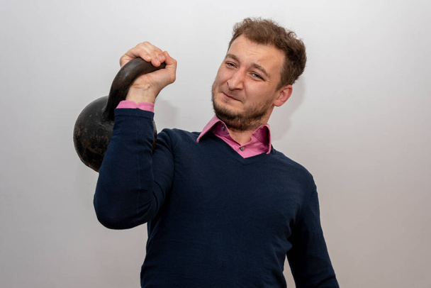 Πορτραίτο ενός άνδρα 35-38 ετών, που σηκώνει ένα βαρύ βάρος σε ένα ελαφρύ φόντο. - Φωτογραφία, εικόνα