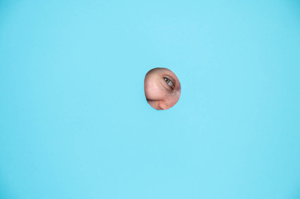 Woman peeking out of hole in blue paper background - 写真・画像
