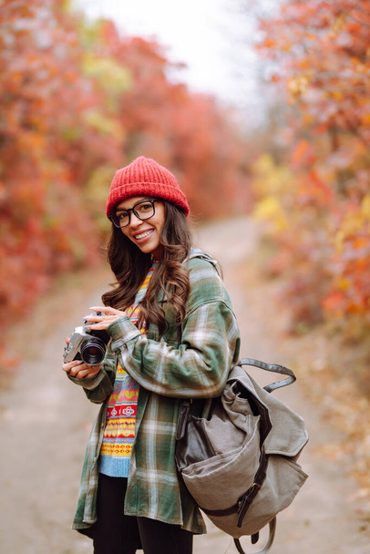 Beautiful woman taking pictures  in the autumn forest. Smiling woman enjoying autumn weather. Rest, relaxation, lifestyle concept. - Foto, afbeelding