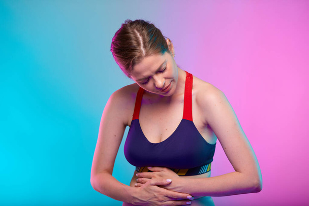 Woman hand on stomach, abdominal pain and digestive disorder. Girl looking down. Female fitness portrait isolated on neon multicolor background. - Foto, Bild