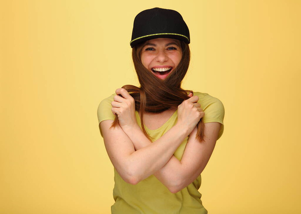 Sorrindo mulher feliz tocando cabelo liso em copo preto isolado no estúdio amarelo de volta. - Foto, Imagem