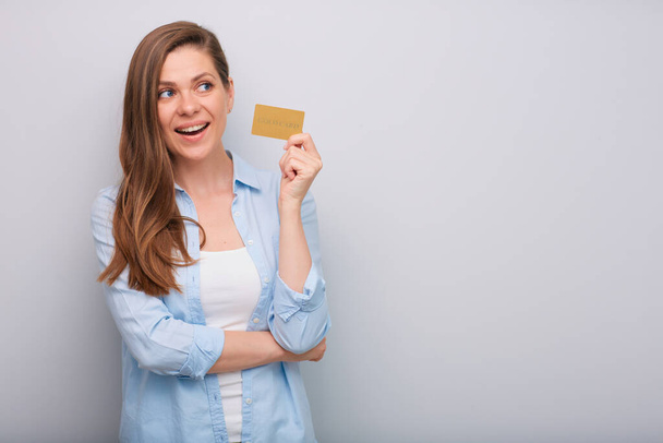 Credit card in hand of smiling woman with long hair looking away dressed blue white shirt isolated portrait   - Fotó, kép