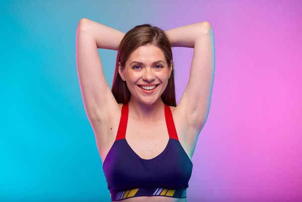 Smiling sporty woman in fitness bra sportswear with hands behind neck. Female fitness portrait isolated on neon colored background. - Φωτογραφία, εικόνα