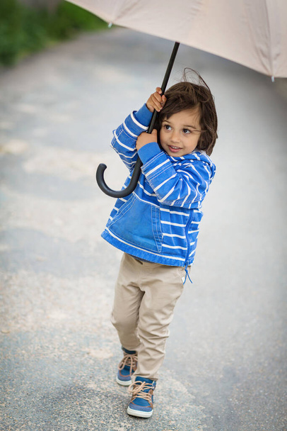 Little eastern handsome baby boy playing with umbrella outdoor in old town. Boy wearing blue jacket - Foto, Bild