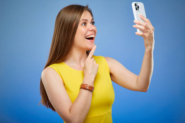 Gülümseyen ve akıllı telefon kullanan mutlu bir kadın. Mavi arka planda izole edilmiş kadın portresi. - Fotoğraf, Görsel