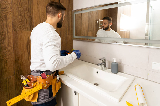 Hombre instalando un espejo en la pared en su baño renovado
. - Foto, imagen