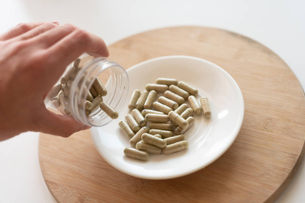 une main versant des pilules de kratom hors du pot en verre à la plaque blanche, mise au point sélective - Photo, image