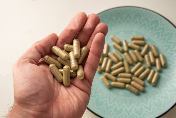 una mano contiene alcune pillole di kratom con piastra verde con altre pillole di kratom sullo sfondo, messa a fuoco selettiva - Foto, immagini