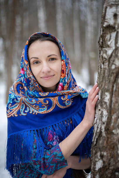 Egy lány a téli erdőben egy Pavloposadsky sálban. A lány átsétál a téli erdőn. Kék tarka sál. Kék Pavloposadszkij sál. - Fotó, kép
