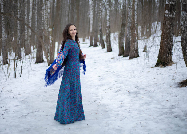 A girl in a winter forest in a Pavloposadsky scarf. The girl walks through the winter forest. Blue motley scarf. Blue Pavloposadsky scarf. - Foto, Imagem