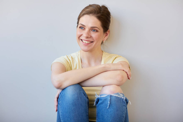Smiling resting woman sits and looks away, isolated portrait in casual  clothes near wall. - Foto, Imagen