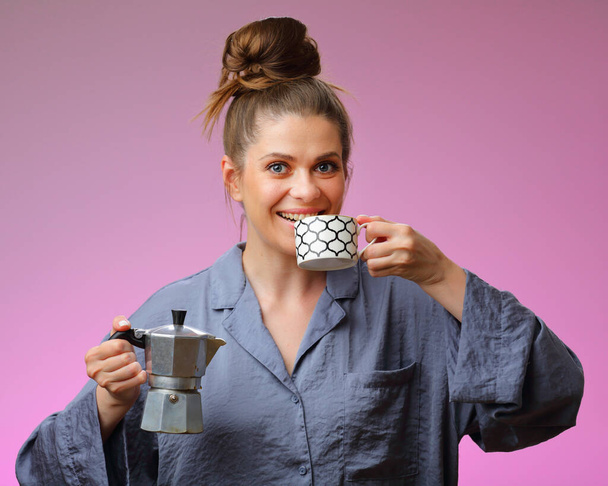Smiling woman pajama dressed drinking coffee and holding geyser coffee maker, isolated on pink female face portrait - Photo, Image