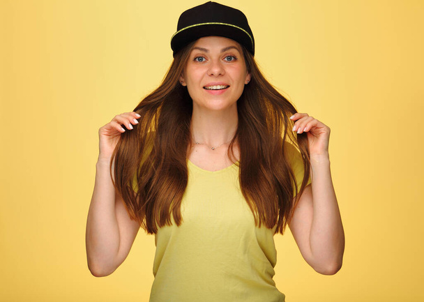 Χαμογελώντας ευτυχισμένη γυναίκα παίζουν με ίσια μαλλιά σε μαύρο κύπελλο απομονώνονται σε κίτρινο. - Φωτογραφία, εικόνα