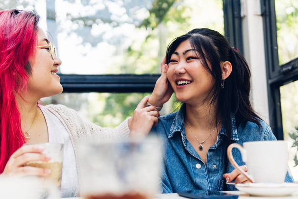 Zwei asiatische Schwestern unterhalten sich in einem Café, lächeln und amüsieren sich. Komplizenschaft zwischen Freunden. - Foto, Bild