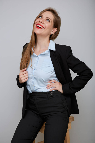Smiling woman in black business suit sitting on tall stool and looking away. Young business woman isolated portrait. - Фото, зображення