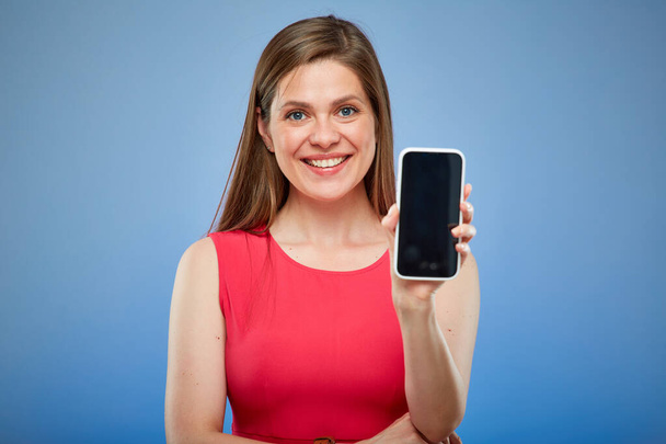 Donna sorridente in abito rosso che tiene smartphone con grande schermo. Persona femminile isolata ritratto su sfondo blu. - Foto, immagini