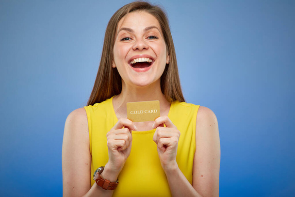 Hppy young woman smiling and holding gold credit card. Isolated female portrait on blue background. - Φωτογραφία, εικόνα