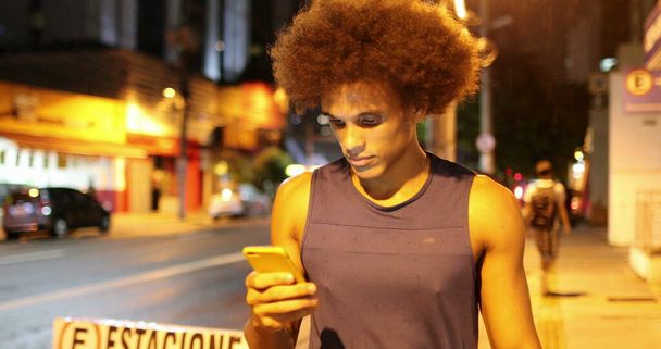 Black african man walking at night in downtown city holding smartphone device - Φωτογραφία, εικόνα