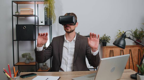 Businessman in suit working using virtual reality futuristic technology VR app headset helmet at home office. Freelancer man busy creating new architecture project. Remote education, study, learning - Photo, Image