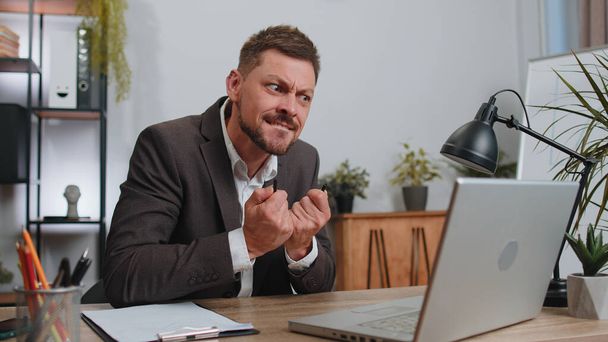 Businessman working on laptop analyzing financial graph decrease loses becoming surprised sudden results, bad news, fortune loss fail at office. Irritated angry freelancer man breaking pencil in hands - Photo, image