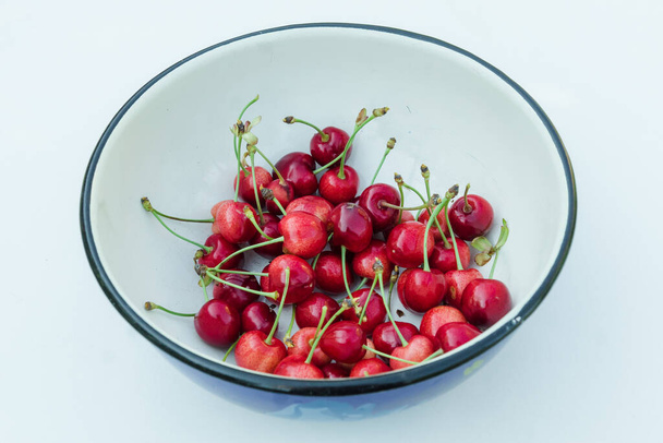 Many red cherry fruits in round bowl, isolated on white. Organic berries fresh. A lot of sweet cherries with petioles top view - Photo, Image