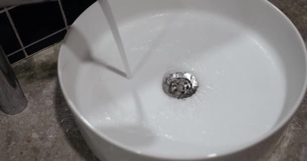 クロムの蛇口からの水の流れは、白いシンク、クローズアップに注ぐ。現代的な浴室の据え付け品 - 映像、動画