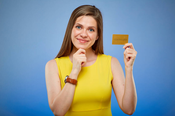 Woman smiling and holding gold credit card. Isolated female portrait on blue background. - Фото, зображення