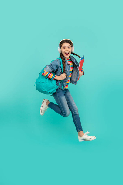 Excited schoolgirl jumping blue background, education. Energetic teenage girl screaming in midair. School education. Informal and non-formal education. - Photo, Image