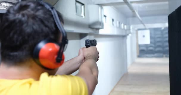 Bir adam atış poligonundaki bir hedefe tabancayla ateş ediyor, arkadan bakıyor, yakın plan. Atış talimi için ön gösteriler - Video, Çekim