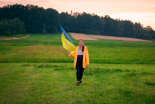 ウクライナの大規模なフラグを持つフィールド内のウクライナの女性。愛国的な写真だ。英雄性と自由。コンセプト。黄色のレインコートの美しい女性。旅行 - 写真・画像