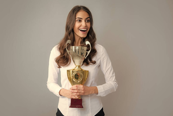 Portrait of happy young business woman with gold trophy cup on gray background - Fotoğraf, Görsel