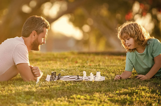 father and son playing chess in morning park. fathers day. happy family. parenthood and childhood. checkmate. spending time together. strategic and tactic. tutorship. dad and kid play logic game. - Foto, immagini