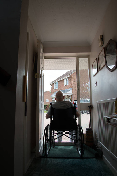 Вид сзади пожилого мужчины девяностых годов, страдающего слабоумием, не способного покинуть дом из-за риска заражения ковоидом-19, любит сидеть в дверях в хорошую погоду. - Фото, изображение