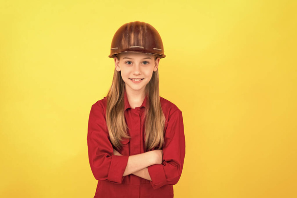 positive teen child in builder helmet on yellow background. - Zdjęcie, obraz