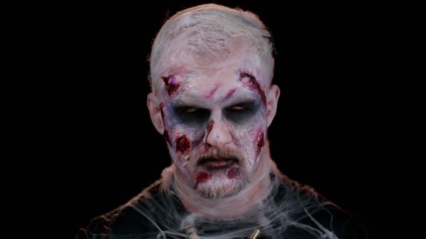 Creepy man with bloody scars face, Halloween stylish zombie make-up. Scary wounded undead guy making faces, looks at camera and smiles terribly. Voodoo rituals. Thematic party. Sinister beast, monster - Footage, Video
