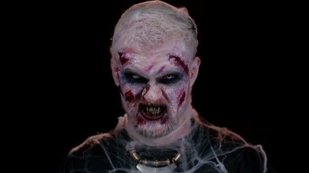 Zombie man met make-up met nep wonden littekens en witte contactlenzen kijken naar camera en schreeuwen, proberen om bang te maken in donkere studio kamer. Een sinistere dode. Halloween, filmen, enscenering concept - Video