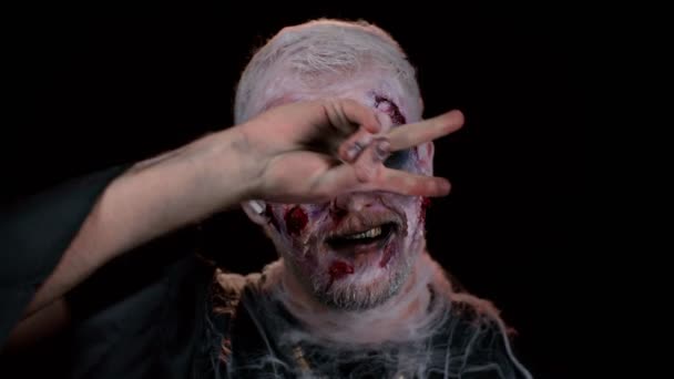 Gruseliger Mann mit blutverschmiertem Halloween-Zombie-Make-up trägt Kopfhörer, hört Musik, tanzt, feiert. Horror-Thema. Finsterer Untoter isoliert auf schwarzem Hintergrund im Studio. Voodoo - Filmmaterial, Video