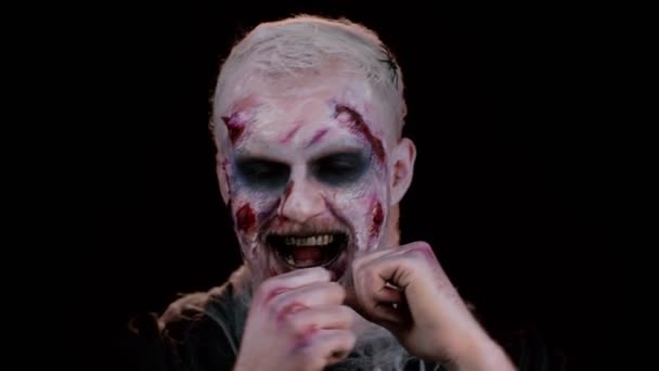 Portret złowrogiego mężczyzny w karnawałowym kostiumie Halloween szalonego zombie słuchającego muzyki, uśmiechającego się tańczącego do muzyki disco rytmicznie poruszającego jej dłońmi, bawiącego się. Temat horror cosplay nieumarły potwór - Materiał filmowy, wideo