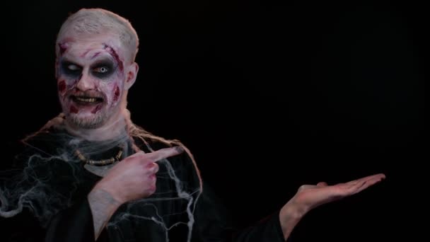 Kanlı suratlı ürkütücü adam, Cadılar Bayramı stili zombi makyajı. Korkunç yaralı ölümsüz adam parmağını uzaya uzatıp işaret ediyor. Reklam logosu için yer. Şeytani canavar. - Video, Çekim