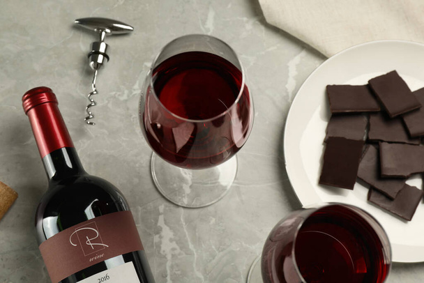 Glasses and bottle of red wine with chocolate on light marble table, above view - Foto, afbeelding
